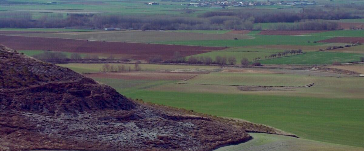 A rural landscape with rolling hills, fields, and a small village in the distance.