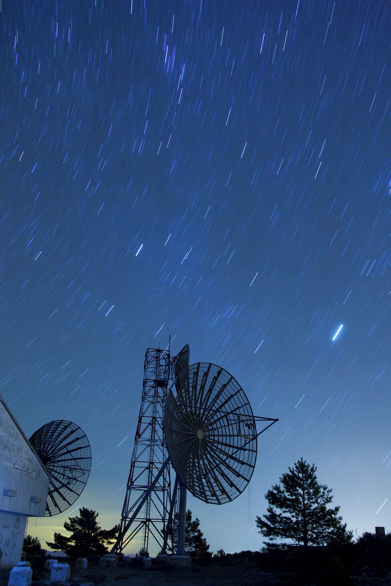 A starry night sky with a large satellite dish and a windmill.