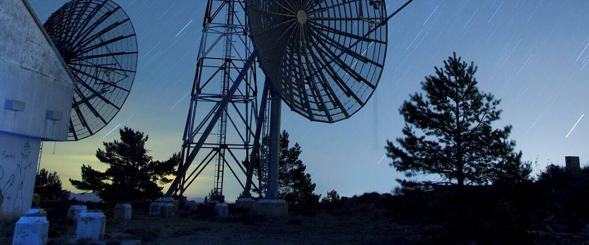 A starry night sky with a large satellite dish and a windmill.
