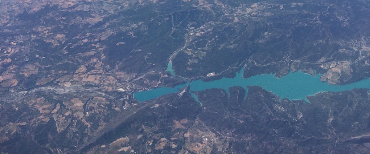 An airplane wing with a logo, a clear sky, and a landscape with fields and a lake.