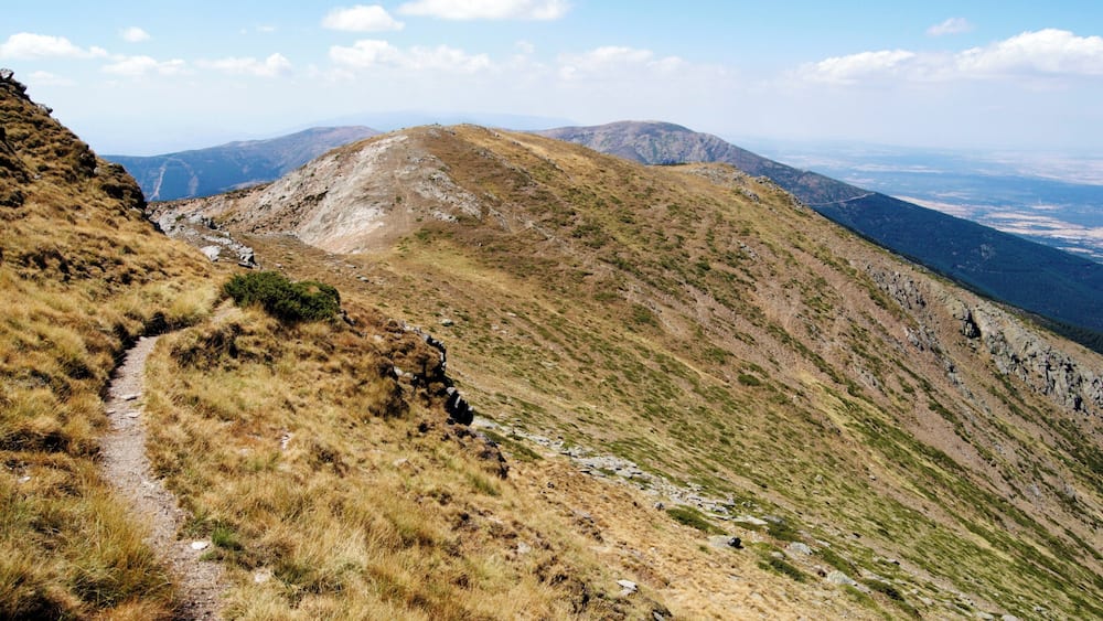 Eine gebirgige Landschaft mit einem Feldweg, der zu einem Berggipfel führt.