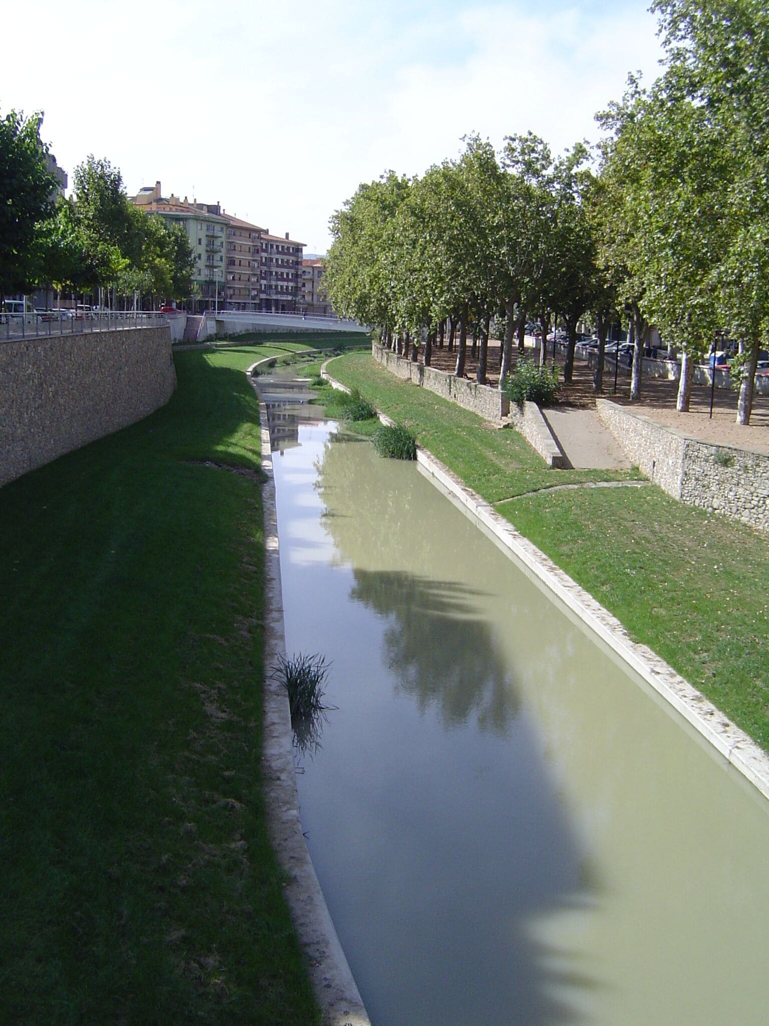A canal with a stone wall on one side and a grassy embankment on the other.