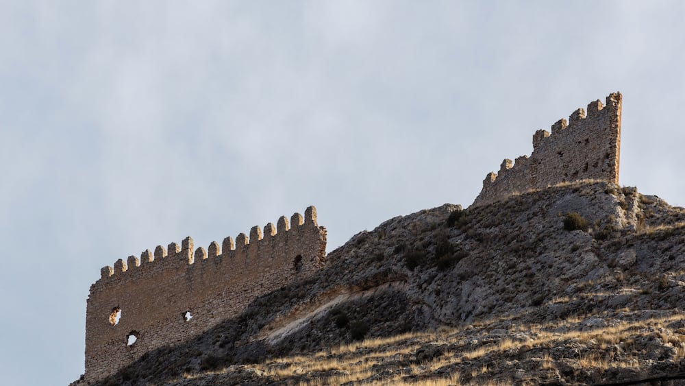 Eine mittelalterliche Steinburg auf einem Hügel mit Zinnen und blauem Himmel.