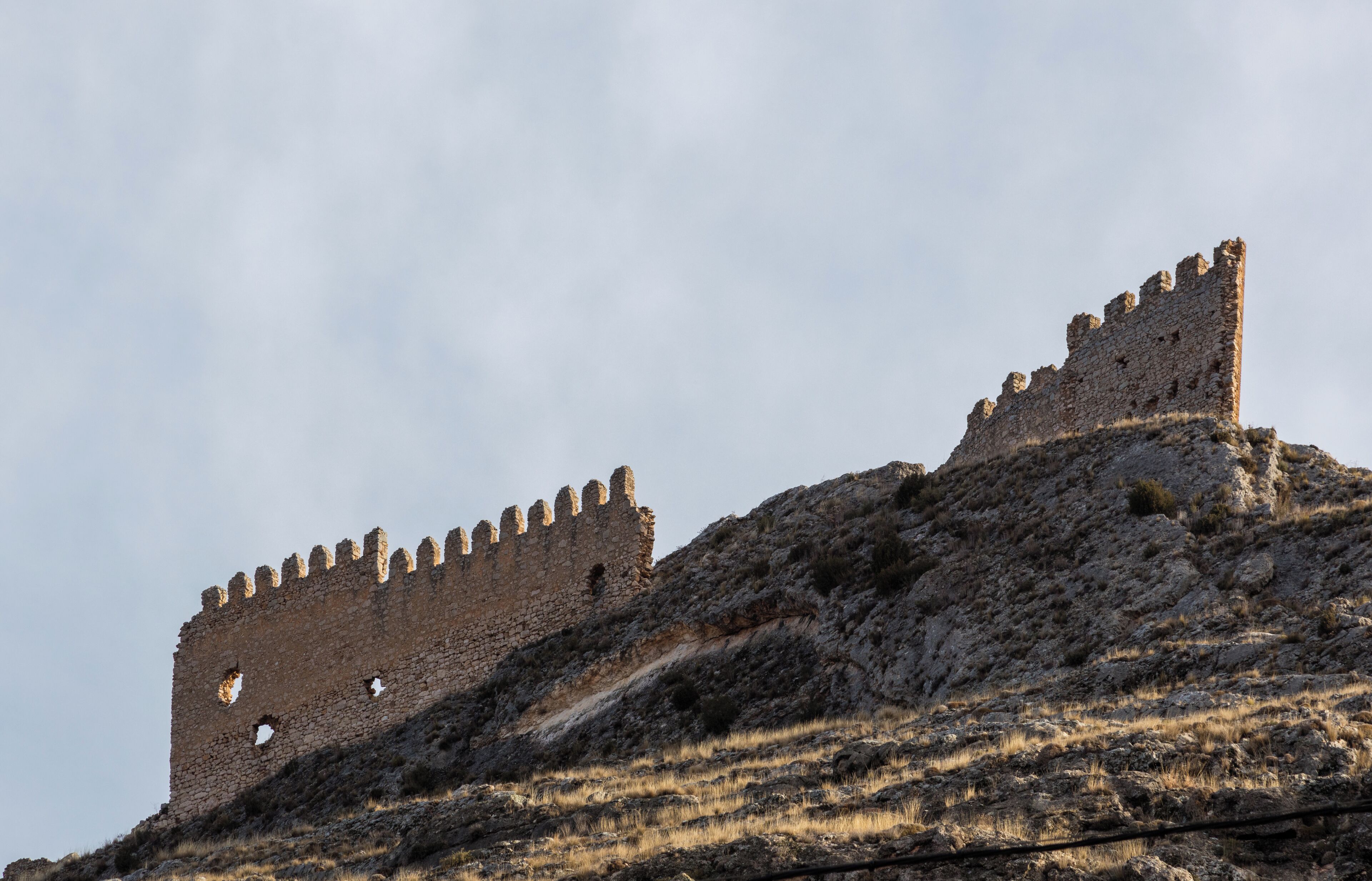 A medieval stone castle on a hill with crenellated walls and a clear sky.