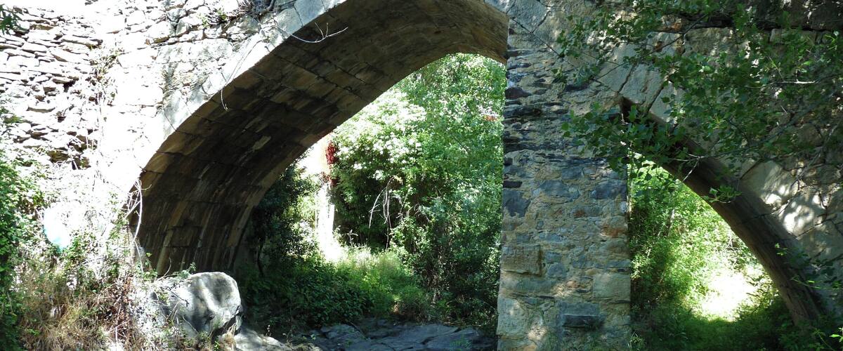 An old stone bridge arching over a stream, surrounded by lush greenery and trees.