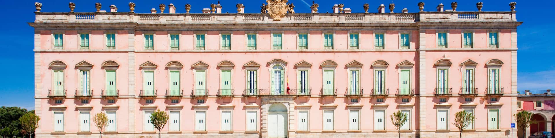 A pink building with green shutters and a large open plaza in front.