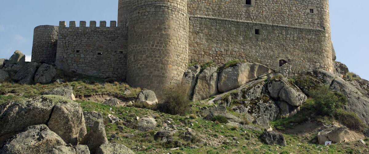A medieval stone castle with multiple towers and battlements, situated on a rocky hill with sparse vegetation.