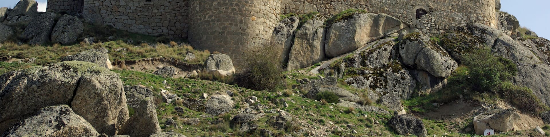 A medieval stone castle with multiple towers and battlements, situated on a rocky hill with sparse vegetation.