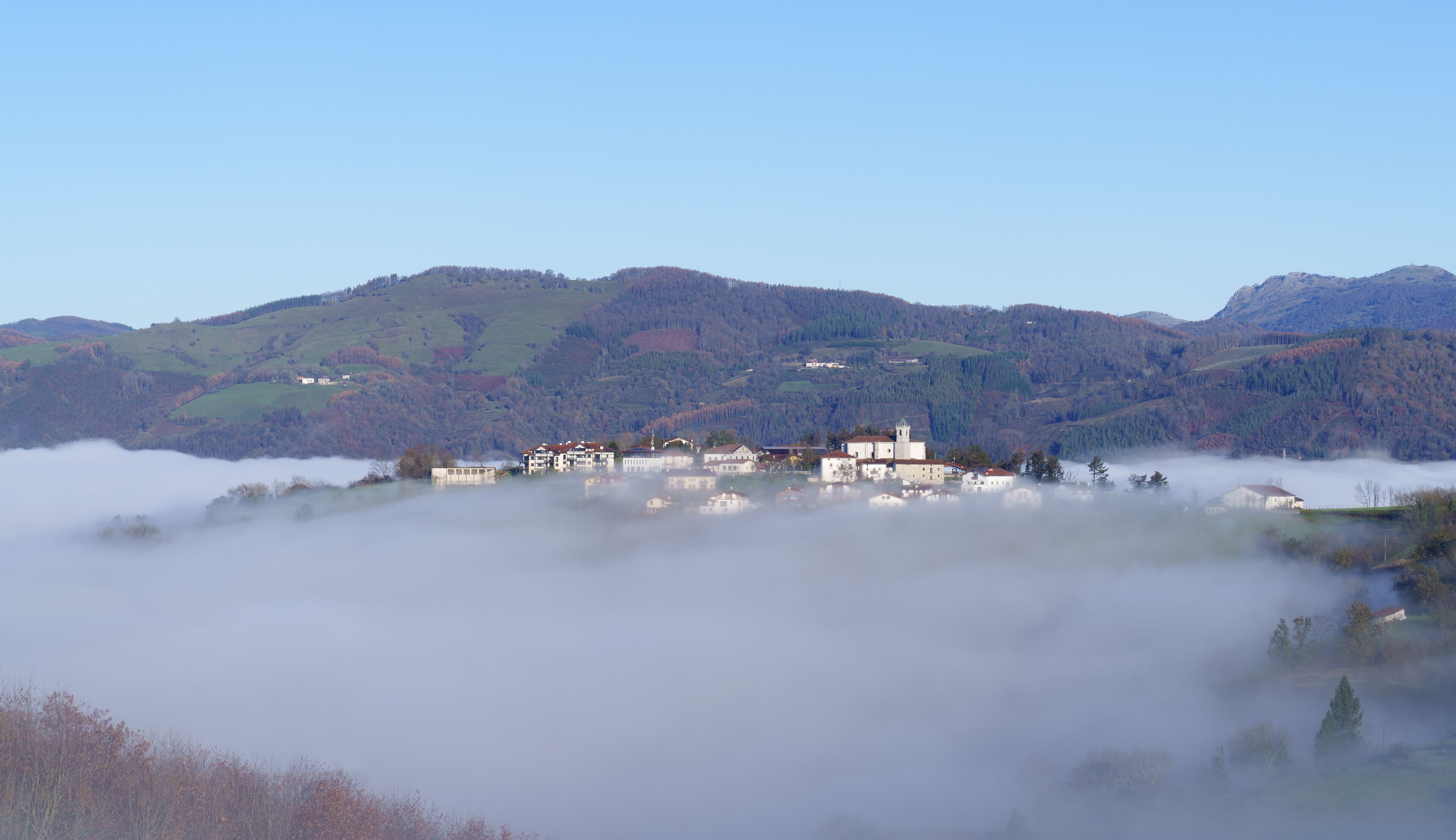 A village nestled in a valley with mist-covered mountains in the background.