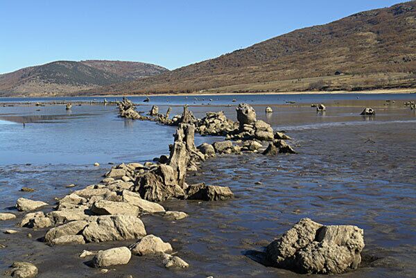 A rocky shoreline with a clear blue sky and distant hills.