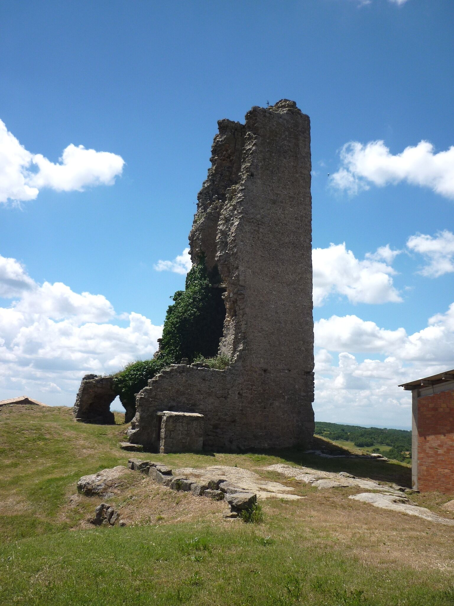 A tall, weathered stone tower with a cross on top, surrounded by grassy fields and a clear blue sky.