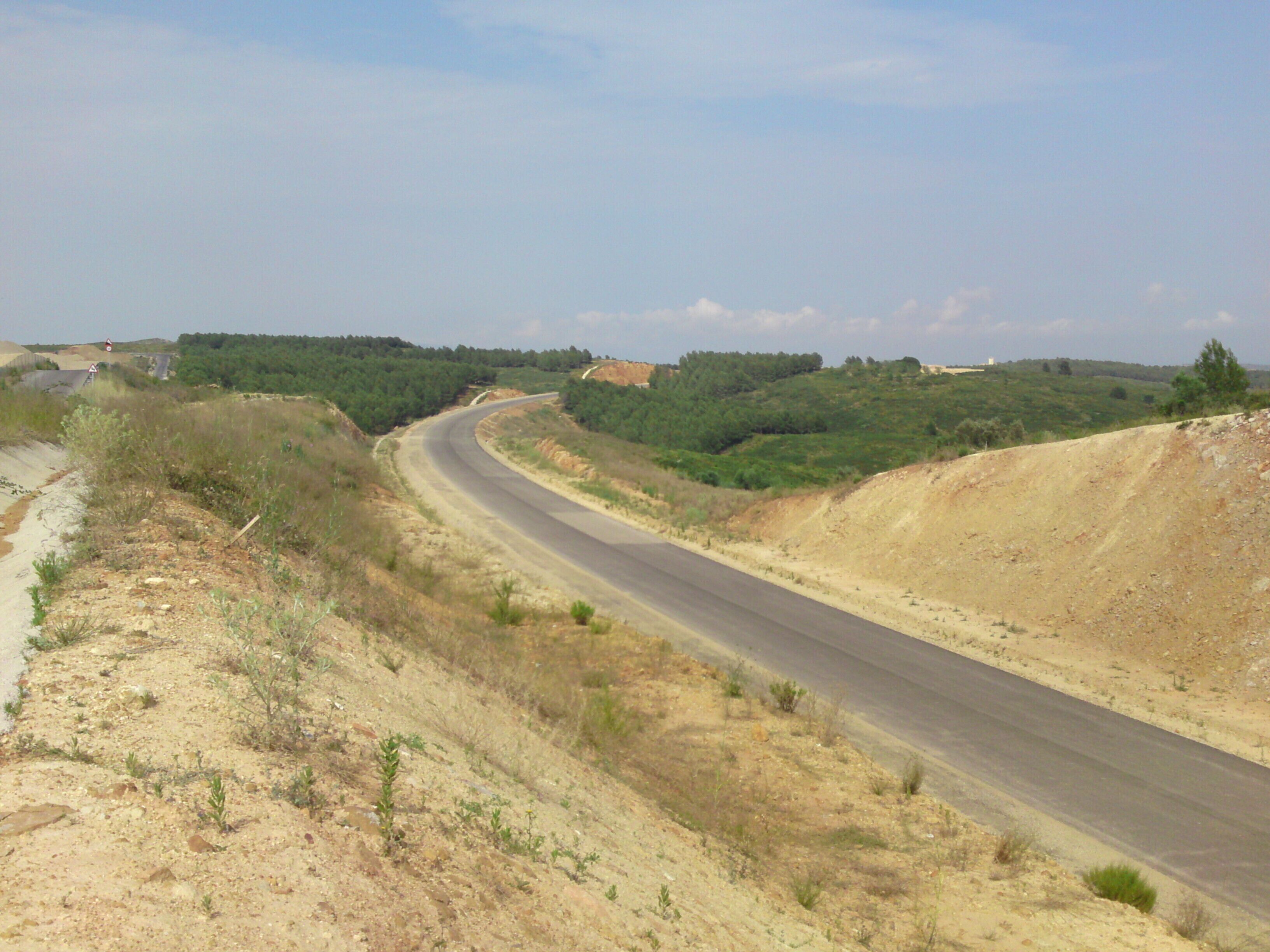 A winding road through a hilly landscape with sparse vegetation and a clear sky.