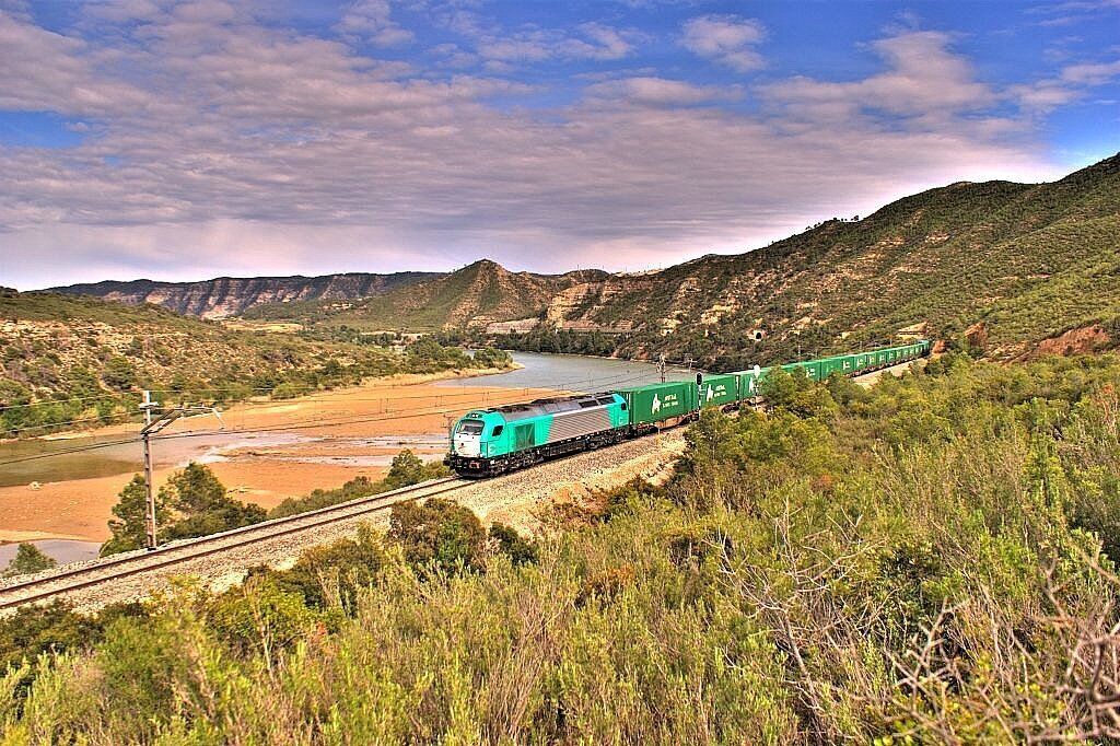 A train traveling through a mountainous landscape with a river and greenery.