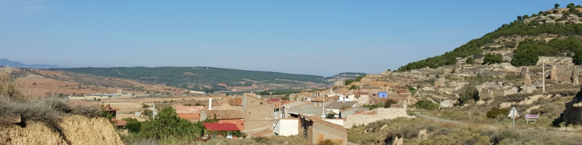 Paisaje rural con un camino serpenteante, casas dispersas y una colina con ruinas.