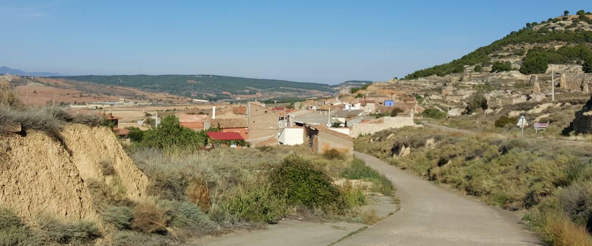 A rural landscape with a winding road, scattered houses, and a hill with ruins.