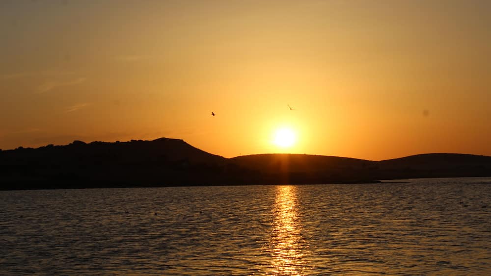 A sunset over a body of water with hills in the background.