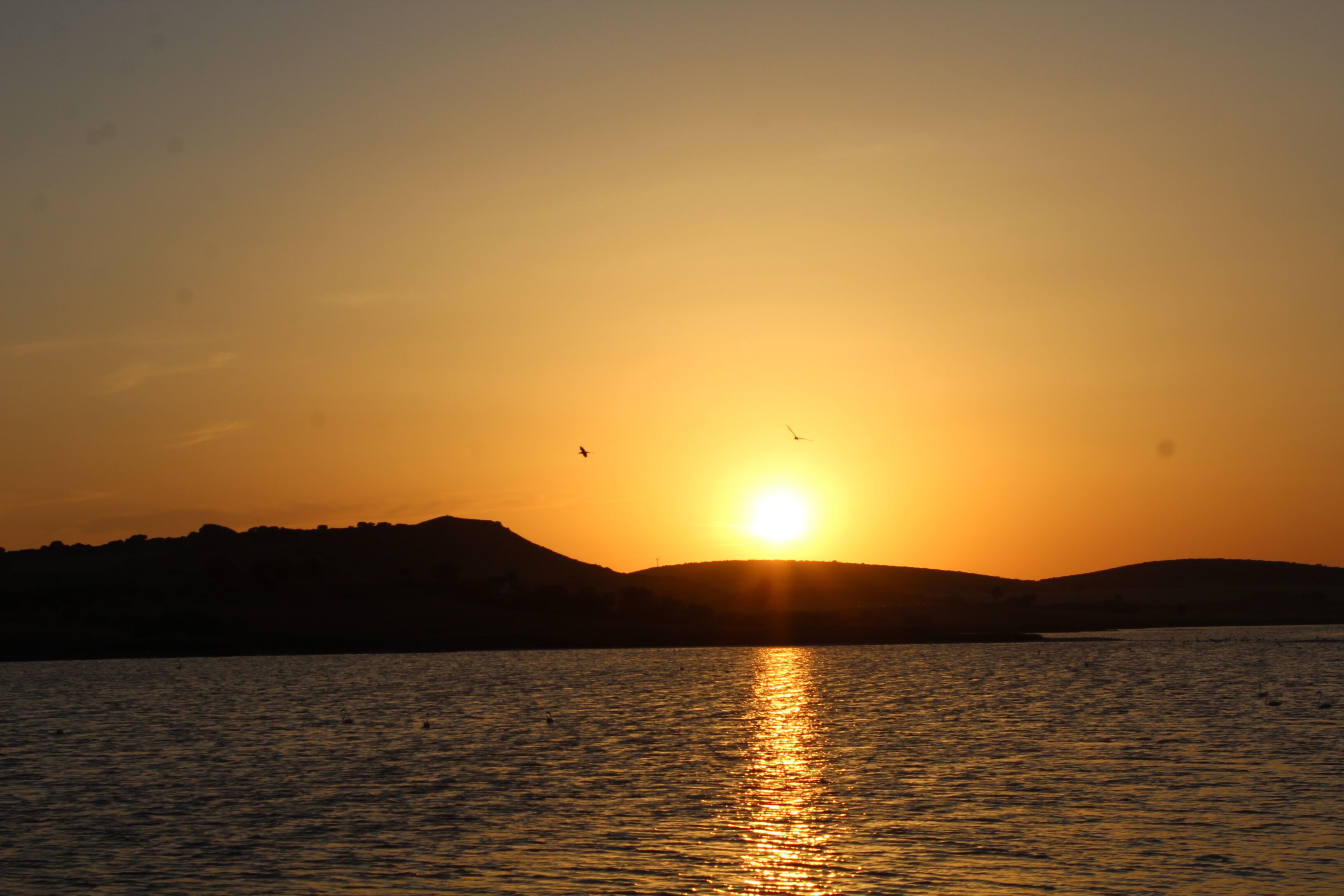 A sunset over a body of water with hills in the background.