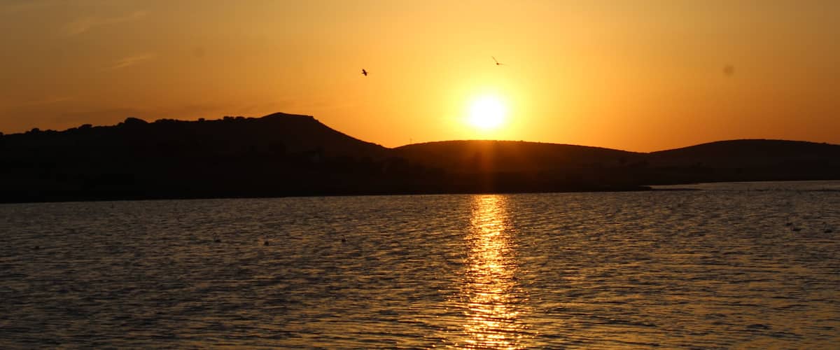A sunset over a body of water with hills in the background.