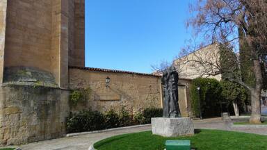 A stone building with a statue in front, a green lawn, and a clear blue sky.