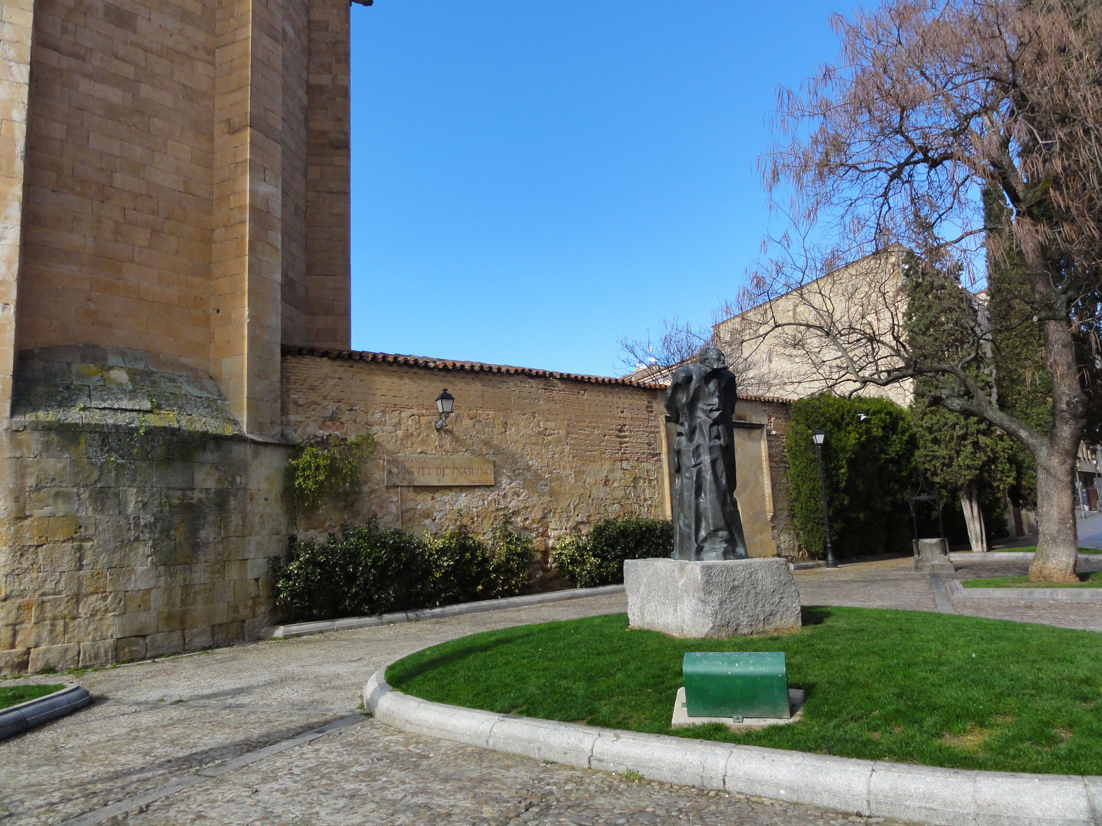 A stone building with a statue in front, a green lawn, and a clear blue sky.