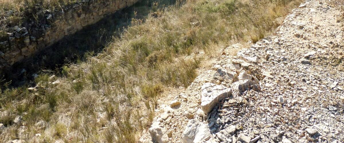 A stone wall and a dry field with sparse vegetation.