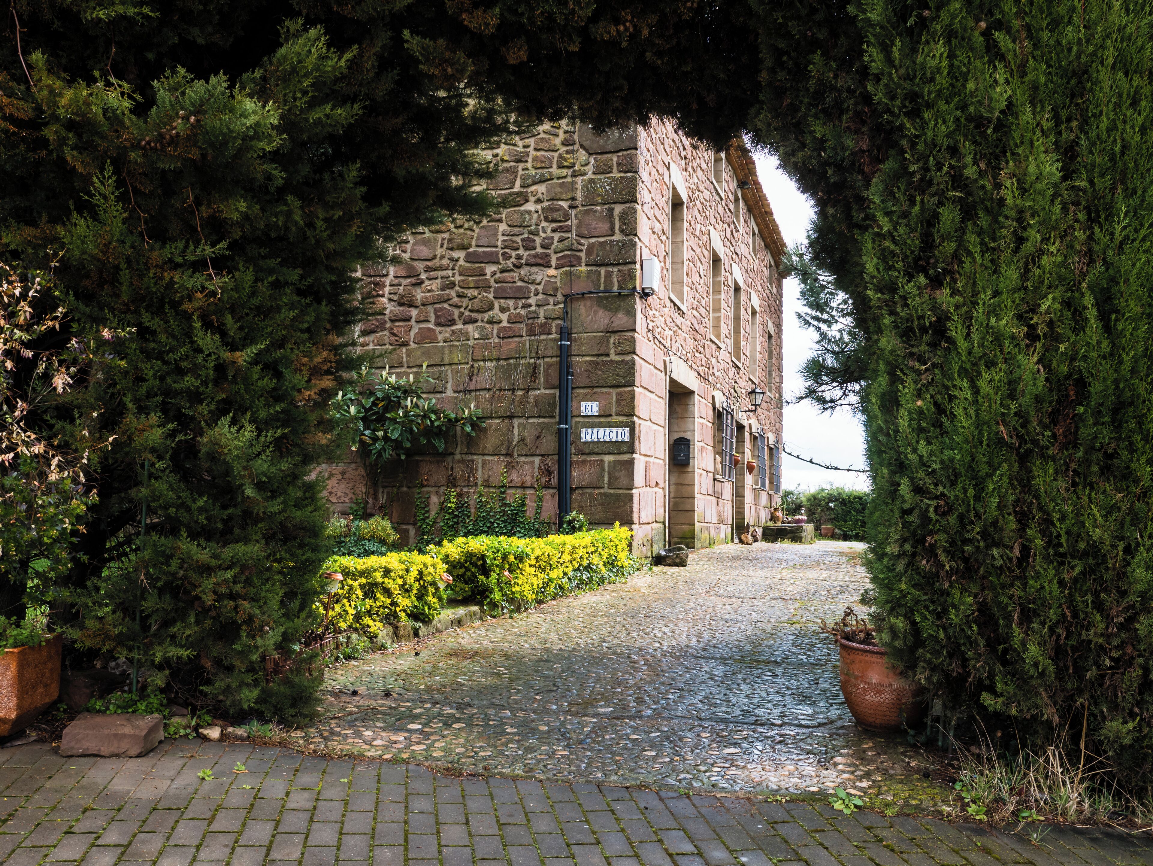 A cobblestone path leading to a stone building with a sign reading "El Pilicio".