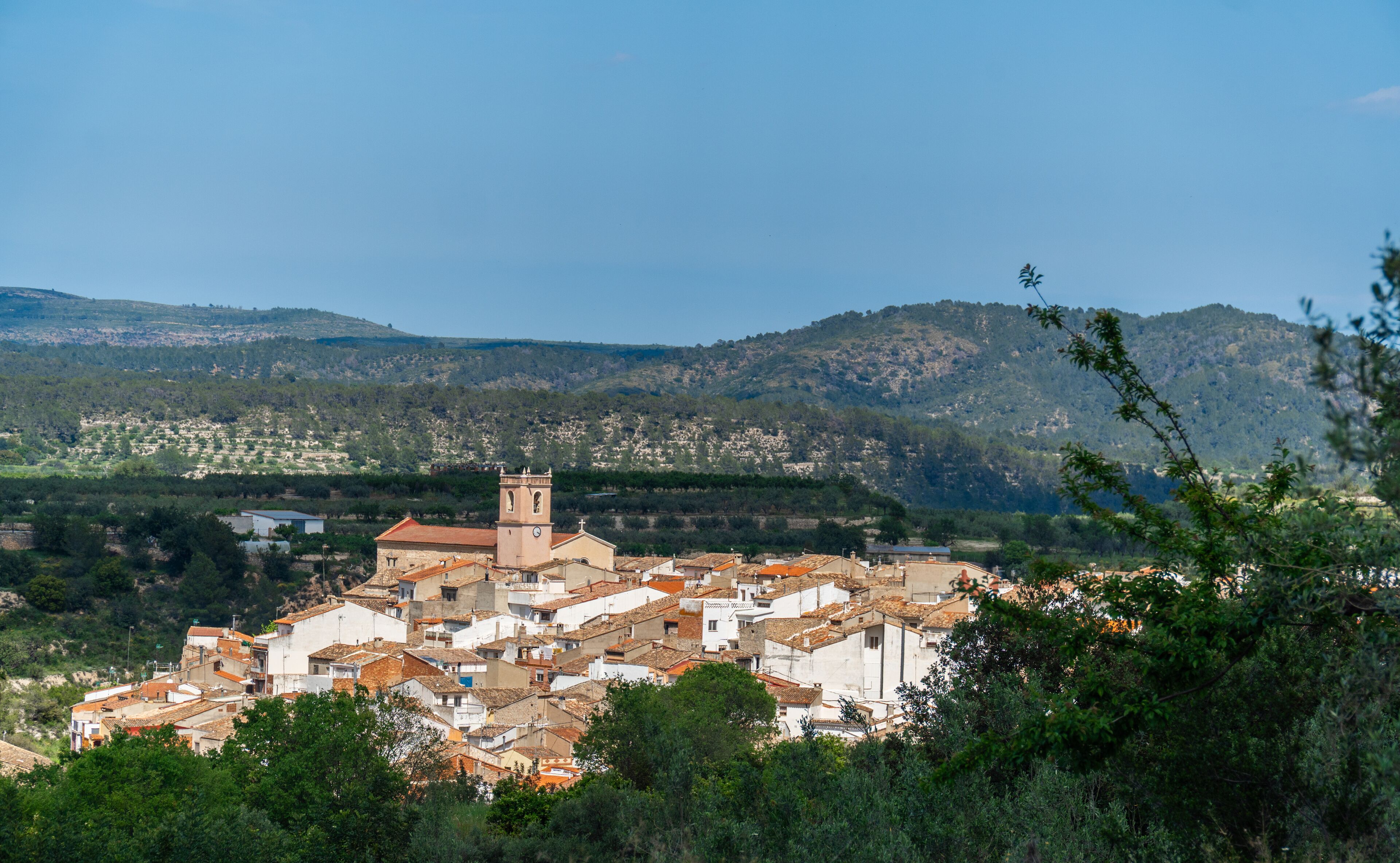 A town with a prominent church tower, surrounded by hills and dense greenery.