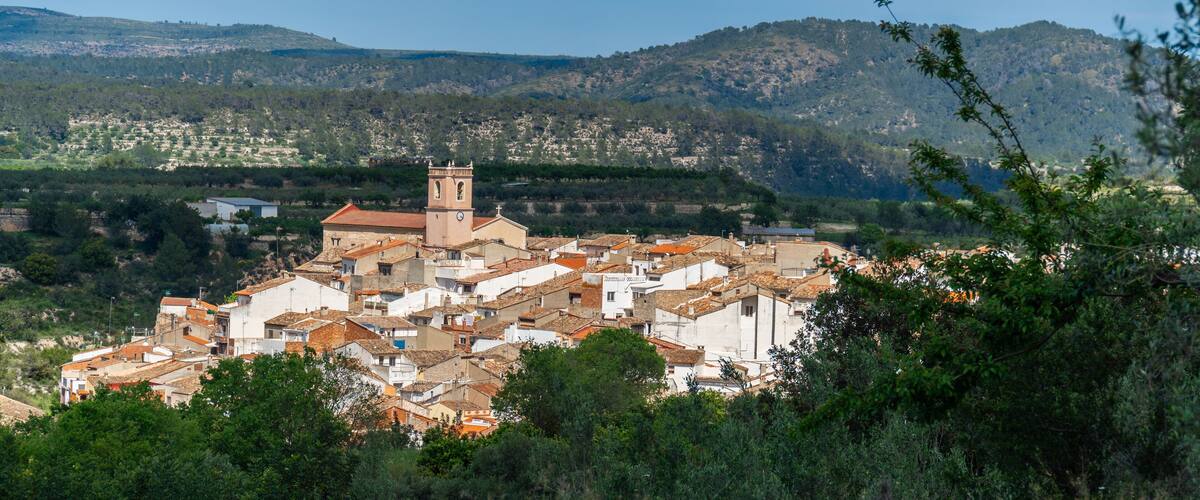 A town with a prominent church tower, surrounded by hills and dense greenery.