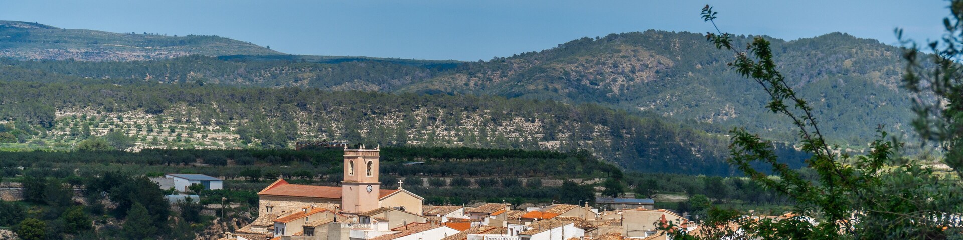 A town with a prominent church tower, surrounded by hills and dense greenery.