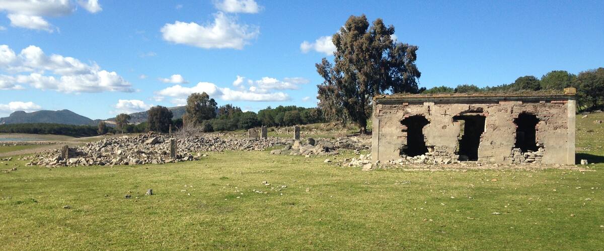 A grassy field with ancient ruins, including a stone structure with arched openings, under a clear blue sky.