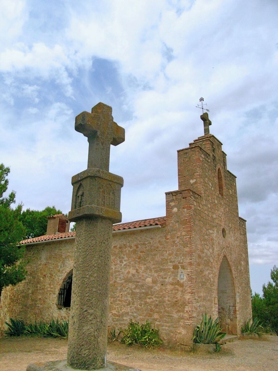 A stone church with a cross, a bell tower, and a weather vane.