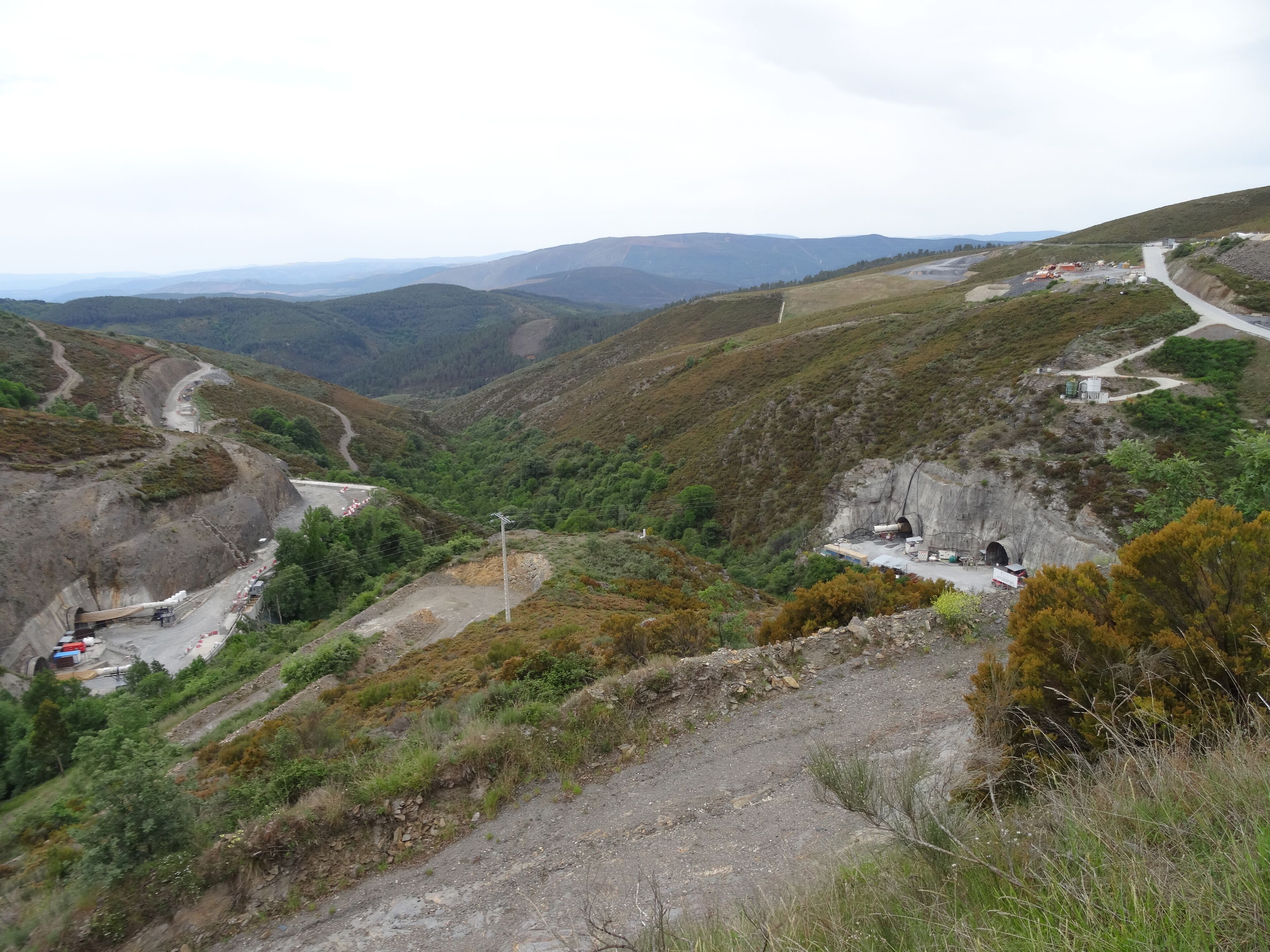 A mountainous landscape with a winding road, a tunnel entrance, and construction equipment.
