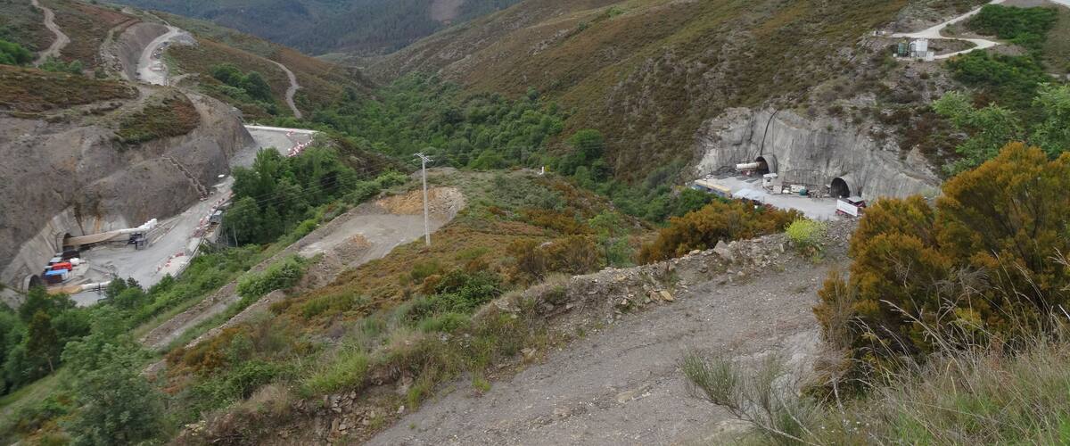 A mountainous landscape with a winding road, a tunnel entrance, and construction equipment.