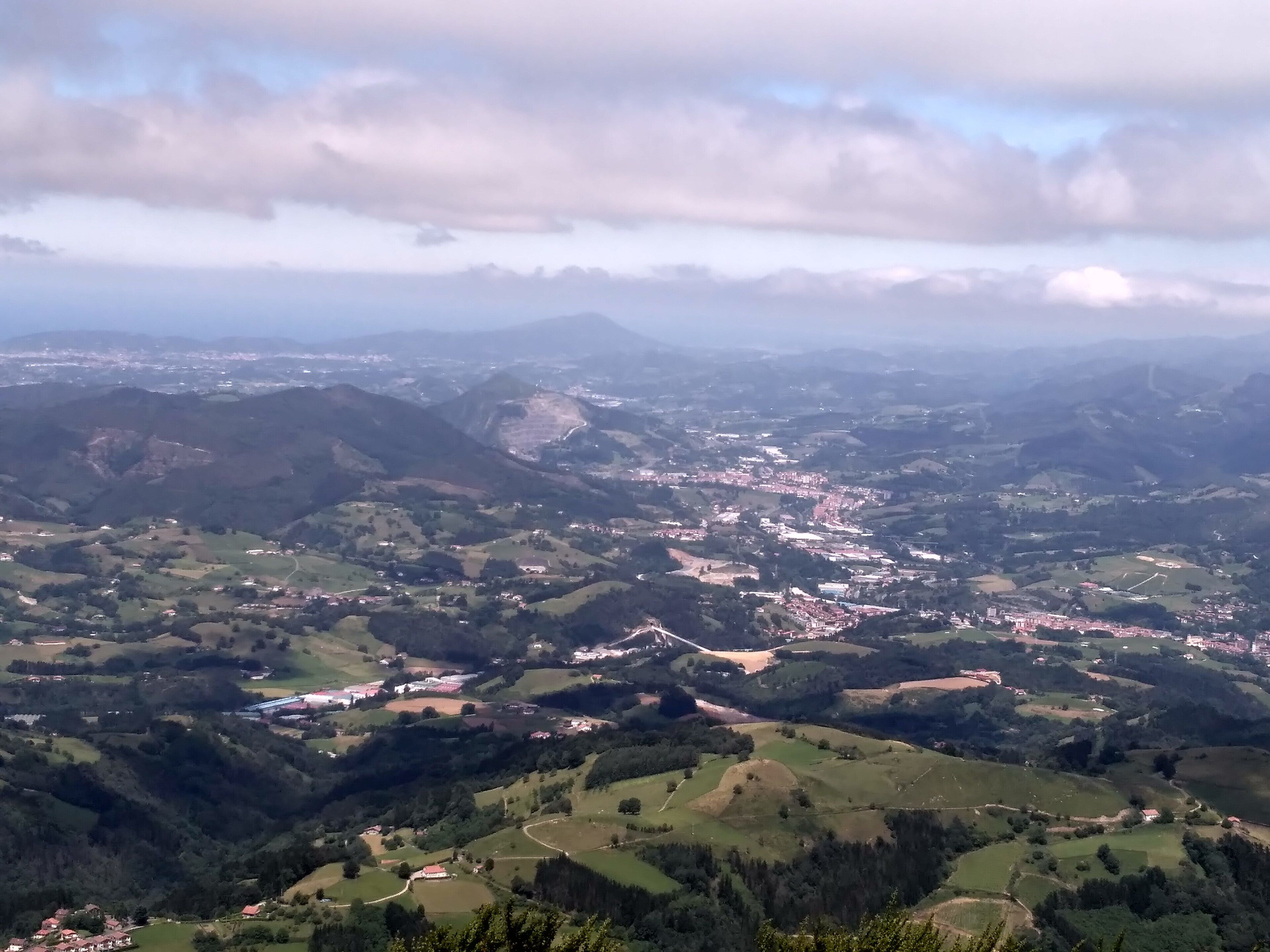 A panoramic view of a valley with rolling hills, scattered houses, and a distant town.