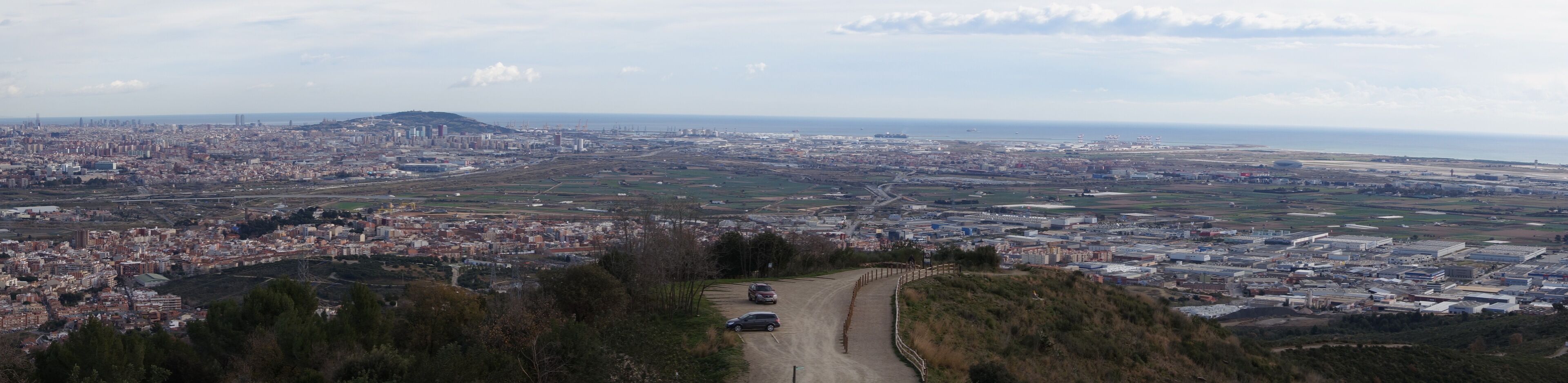 A coastal cityscape with a prominent hill, a large body of water, and a winding road leading towards the city center.