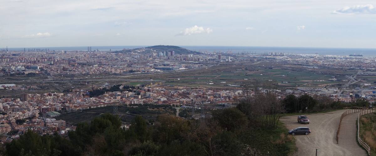 A coastal cityscape with a prominent hill, a large body of water, and a winding road leading towards the city center.