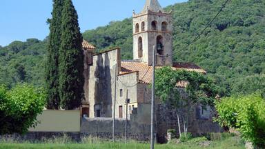 A historic church with a bell tower, surrounded by lush greenery and hills.