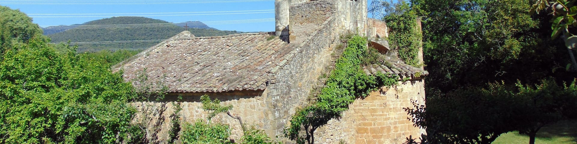 A historic church with a bell tower, surrounded by lush greenery and hills in the background.