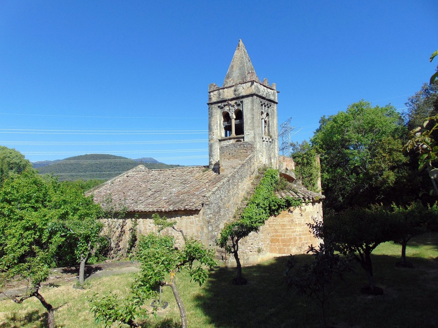 A historic church with a bell tower, surrounded by lush greenery and hills in the background.
