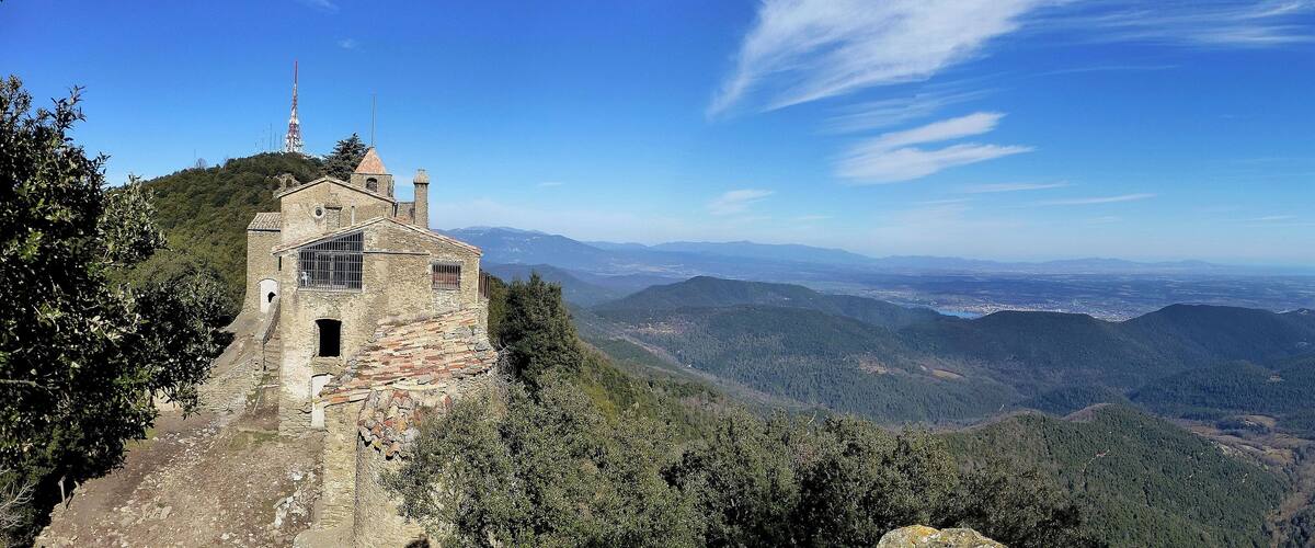 A stone church on a hill with a view of mountains and a clear sky.
