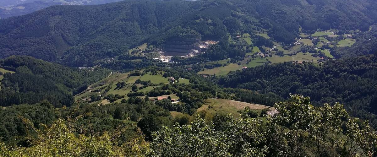 A valley with a lake surrounded by forested hills and distant mountains.