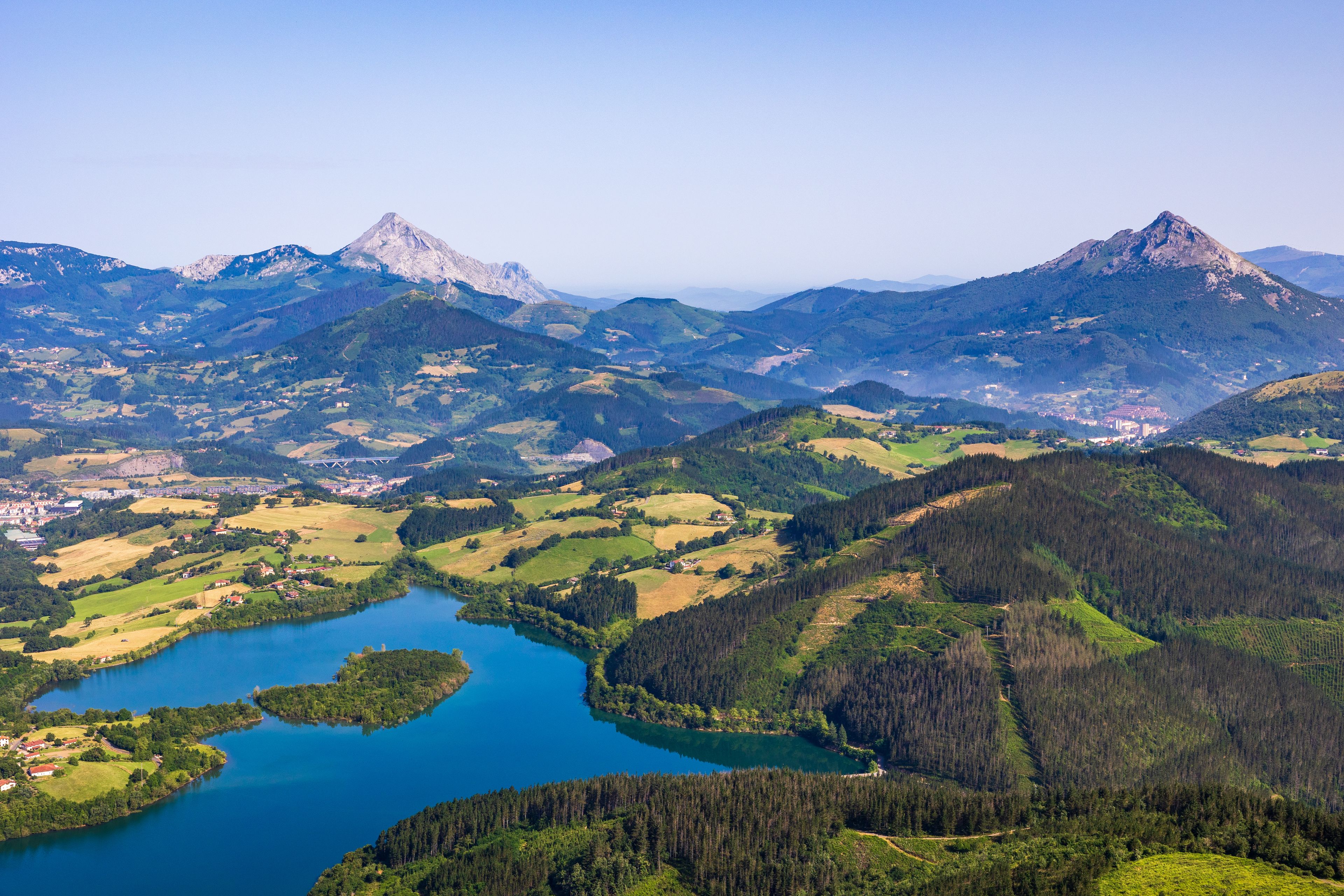 Paisagem montanhosa com um lago cercado por áreas florestais e povoados dispersos.