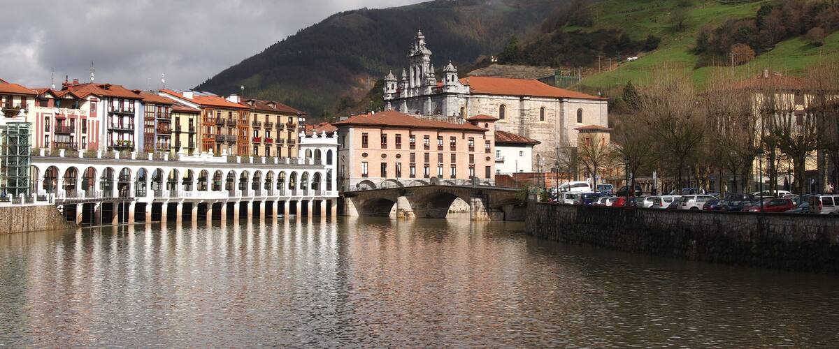 A river with a bridge, historic buildings, and a mountain in the background.
