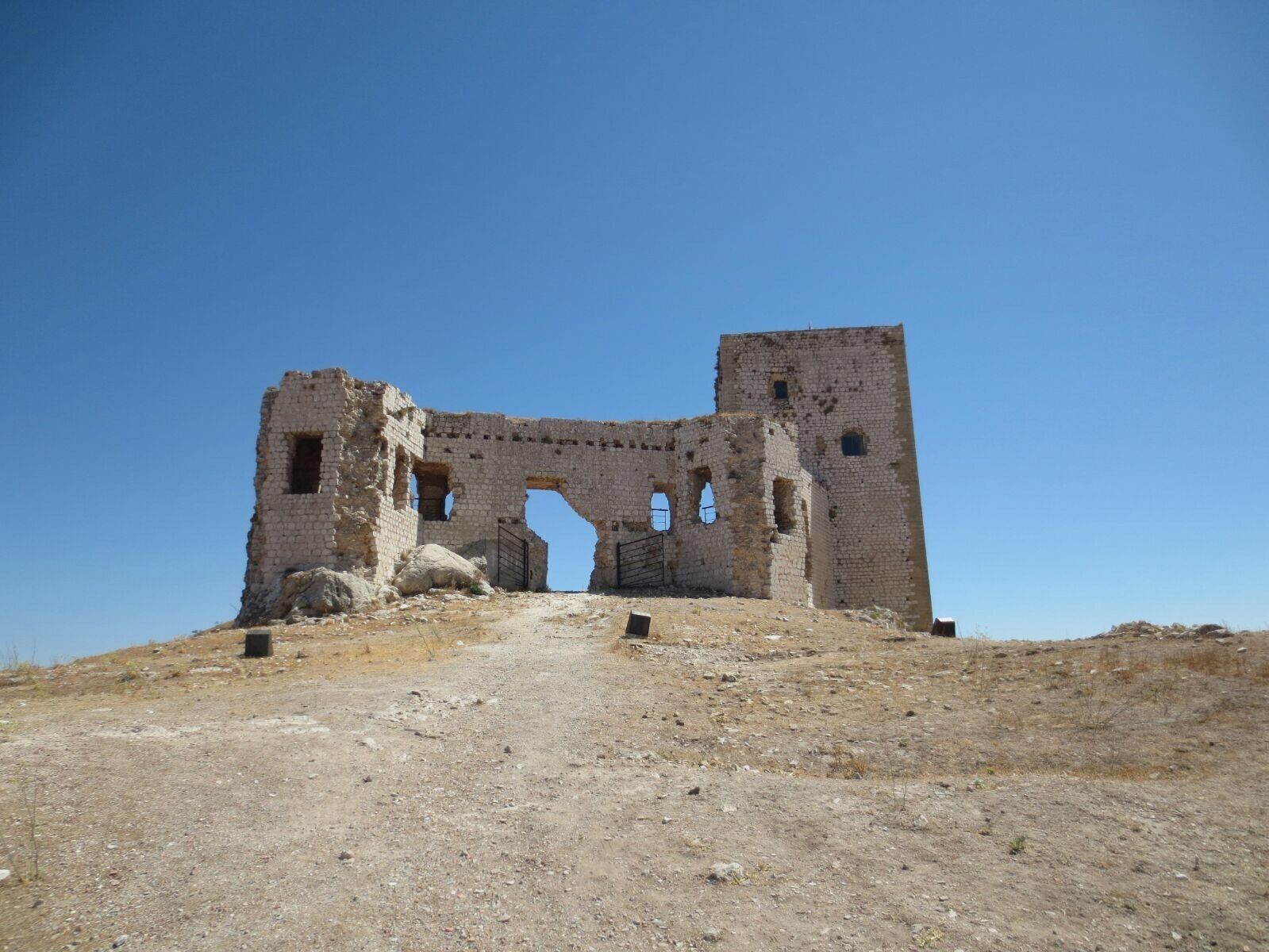 An ancient stone structure with a large archway and a tower, surrounded by a dry, rocky landscape.