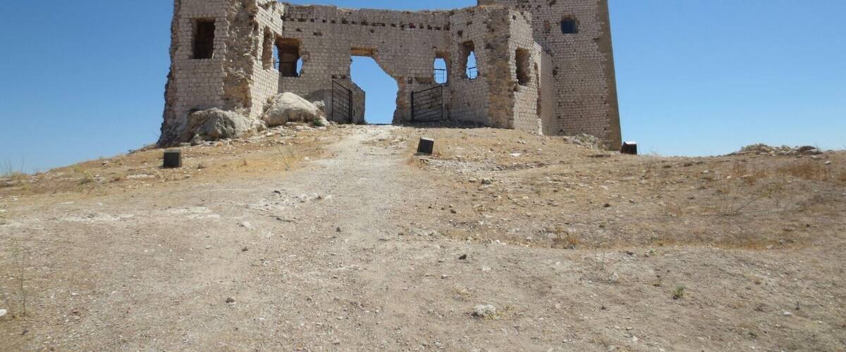 An ancient stone structure with a large archway and a tower, surrounded by a dry, rocky landscape.