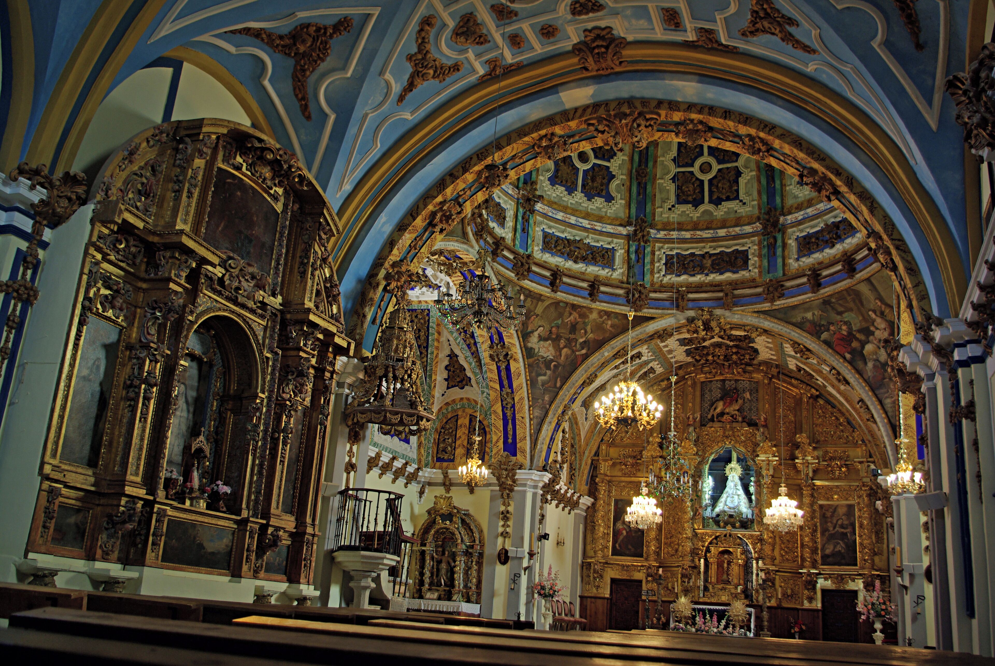 An ornate church interior with detailed gold decorations, a large chandelier, and a central altar.