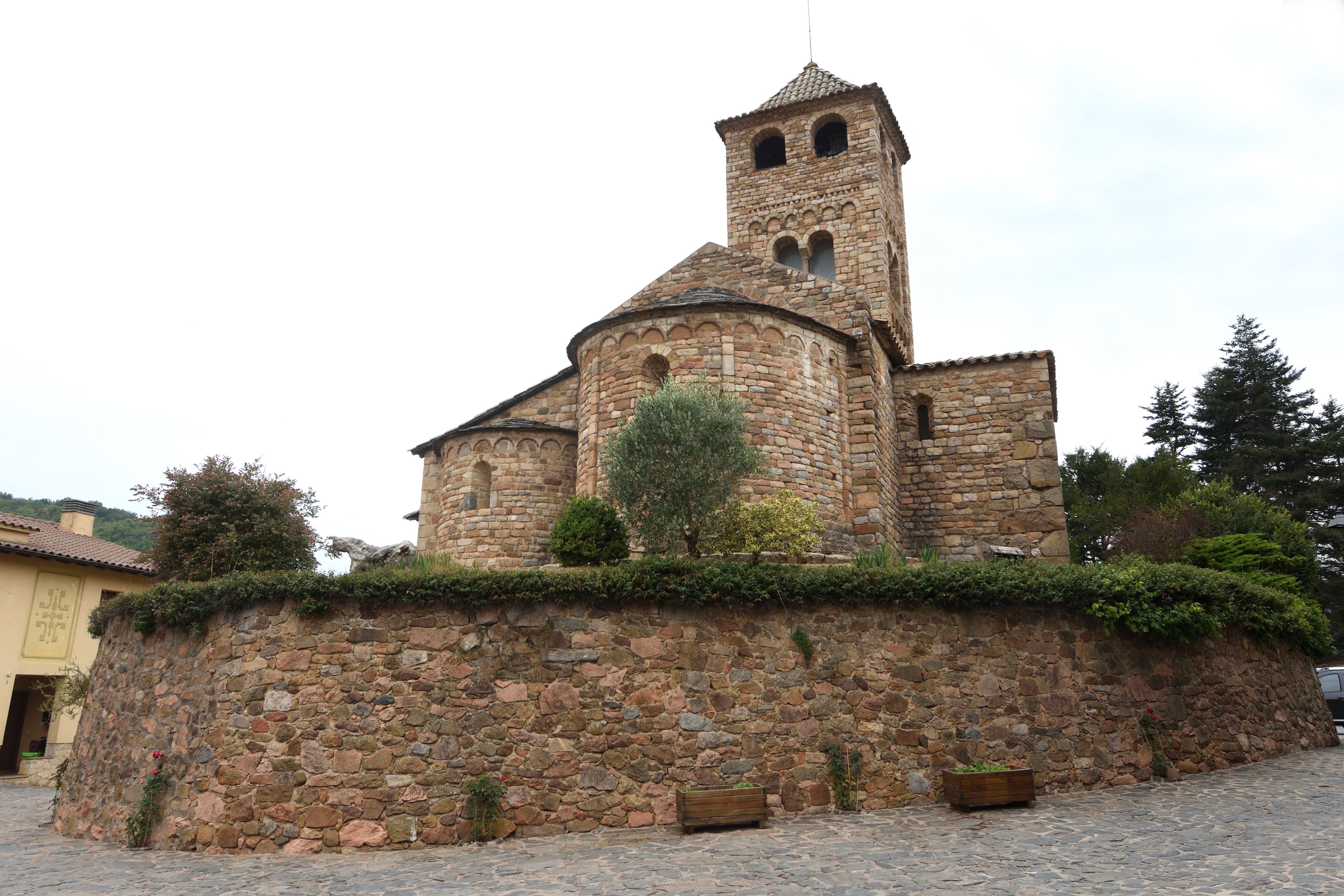 Une église en pierre dotée d’un clocher, entourée d’une cour pavée et de verdure.