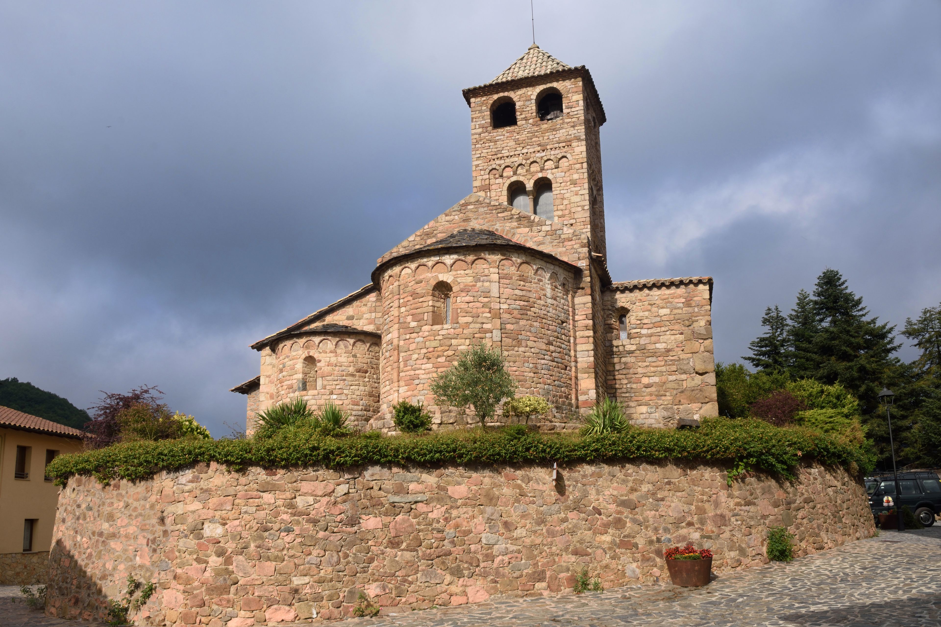 Une église en pierre dotée d’un clocher, entourée de verdure et bordée d’un chemin pavé.