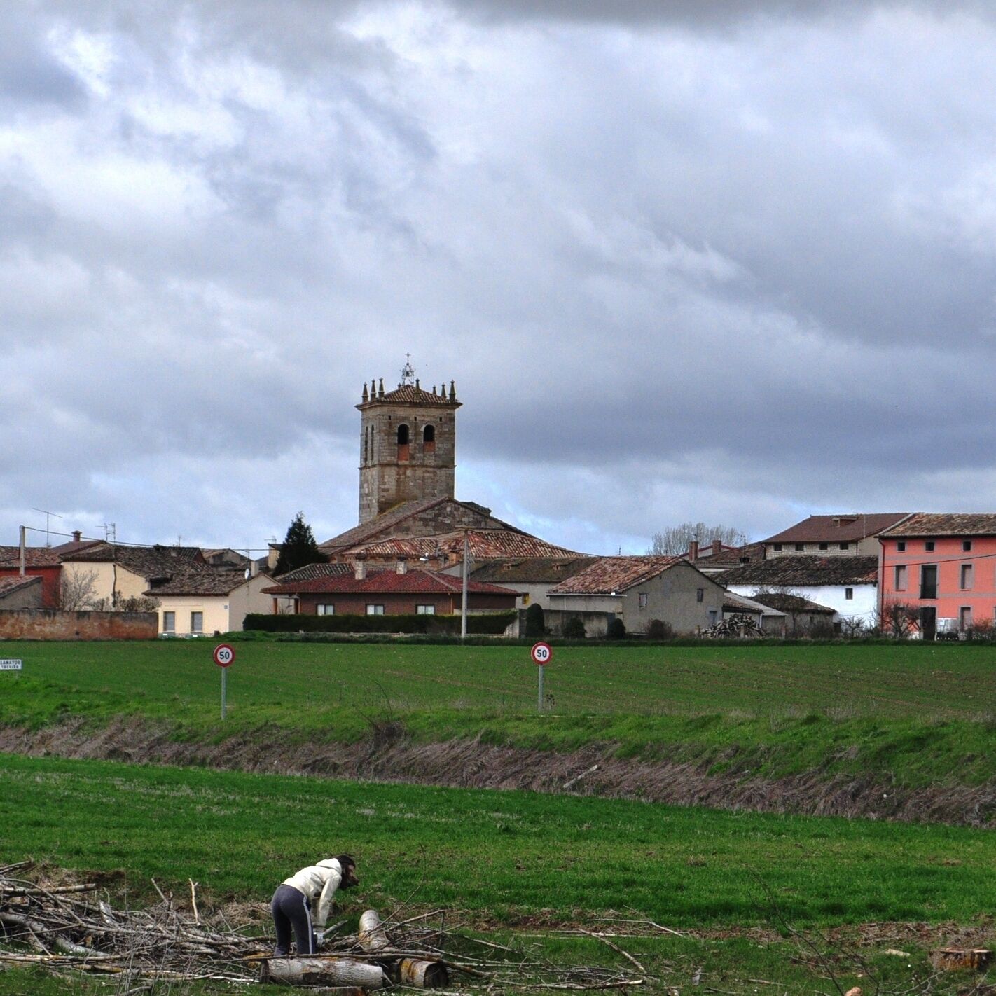 A rural landscape with a tower, houses, and a person working in a field.