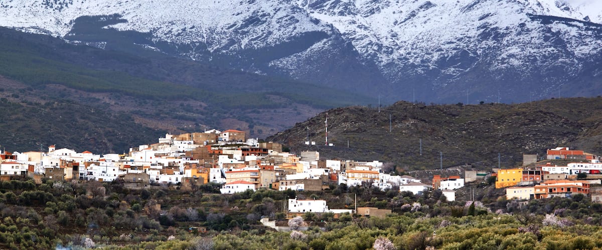 A town nestled at the base of snow-capped mountains, with buildings in white and orange.